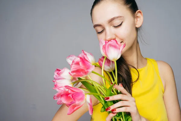 Mooie charmante meisje in een gele jurk geurige roze bloemen ruikt, geniet — Stockfoto