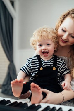 küçük sarışın oğlu onun kollarında holding, piyano, gülen ve having fun kıvırcık Genç Anne