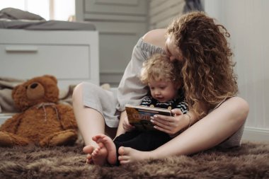 kıvırcık saçlı, nazik anne küçük oğlu ile yere oturur, onu okumak için öğretir, kucaklayan