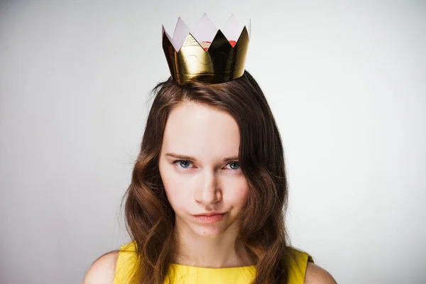 Ein böses junges Mädchen mit blauen Augen blickt in die Kamera, in einem gelben Kleid, eine goldene Krone auf dem Kopf, unzufrieden mit etwas — Stockfoto