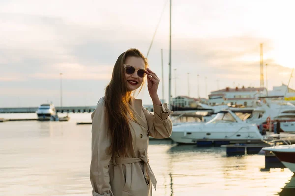 Miła dziewczyna z długimi, grubymi włosami czeka na jej jacht w morze ort, w czarne okulary przeciwsłoneczne — Zdjęcie stockowe