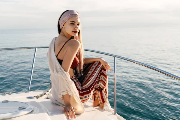 Hermosa joven con ropa elegante sentada en un yate blanco y posando, disfrutando del descanso y las vacaciones de verano —  Fotos de Stock