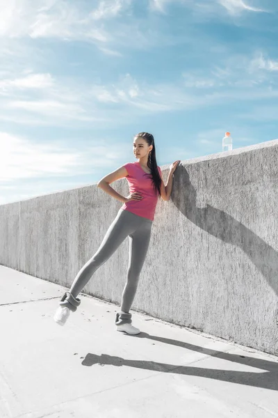 tall slender girl in pink t-shirt doing exercises for leg muscles outdoors, wants a beautiful figure