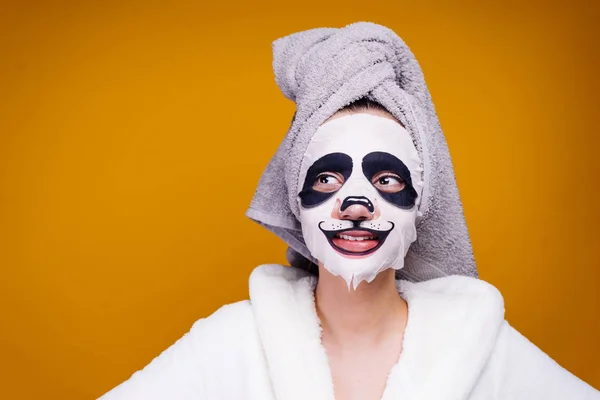 lovely girl with a towel on her head looks after herself, on her face a moisturizing mask with a panda face