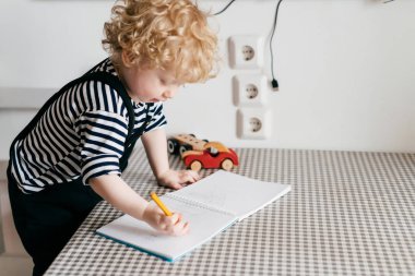 bir defter, bir masada sarışın kıvırcık yürümeye başlayan çocuk çizer