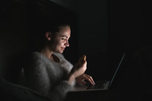 Güzel kız akşamları karanlıkta yatakta oturur, onu laptop komik ILM görünüyor — Stok fotoğraf