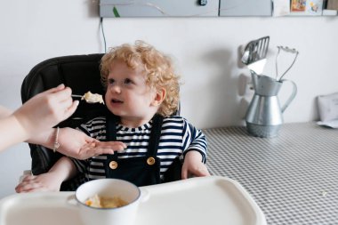 Genç bir anne küçük kıvırcık oğlu yararlı püresi ile beslemeleri bir aile kahvaltı mutfak