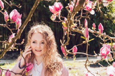 güzel kıvırcık kadın güneş, sıcaklık ve bahar parkında telefonda söz