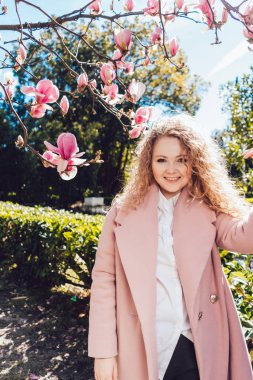 gülümseyen bir beyaz gömlek ve pembe ceket bir parkta güzel kokulu Pembe Manolya zevk lüks kıvırcık kadın