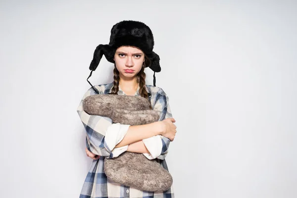 A sad Russian girl in a black fur hat is displeased with something, holding gray winter boots — Stock Photo, Image