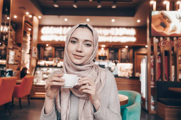 Schöne arabische Mädchen mit Kopftuch auf dem Kopf speist in einem gemütlichen Café, trinkt duftenden Tee — Stockfoto