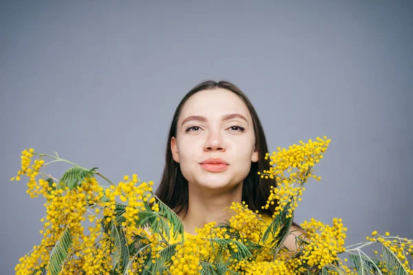 Schöne junge Mädchen mit einer sauberen weißen Haut posiert mit einem Strauß gelb duftender Mimosen — Stockfoto