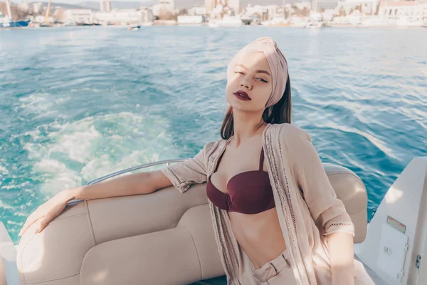 an attractive stylish girl with a headscarf on her head rests and relaxes on her yacht, sails on the blue sea