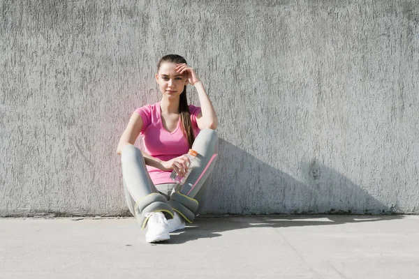 ジョギングの後安静時、太陽の下で地面に座ってピンク t シャツで疲れている若い女の子 — ストック写真