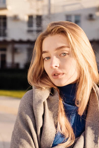 Linda menina de olhos azuis com cabelo loiro posando no jardim ao sol, apreciando o calor da primavera — Fotografia de Stock