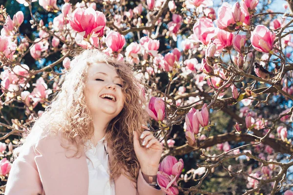 Rizado rizado riendo mujer disfruta de descanso y calidez en el parque, posa al lado de magnolia — Foto de Stock