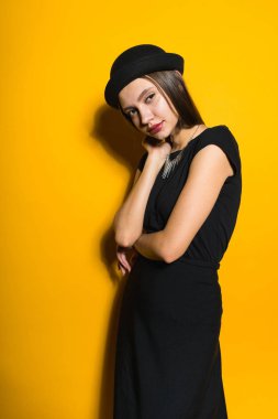 kendine güvenen şık kız model poz sarı zemin üzerine siyah moda şapkalı