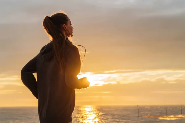 Testarda ragazza dai capelli lunghi corre intorno al mare al tramonto, vuole perdere peso — Foto Stock