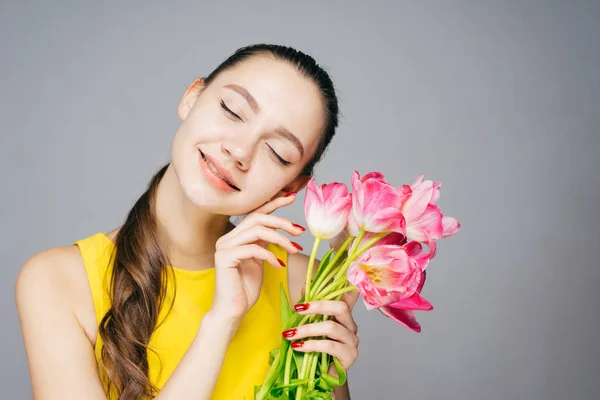 Charmante mooi meisje in een gele jurk glimlachen, sloot haar ogen, houdt een boeket geurende bloemen — Stockfoto