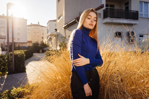Sicuro elegante ragazza modello biondo in un maglione blu in posa su una strada della città al sole — Foto Stock