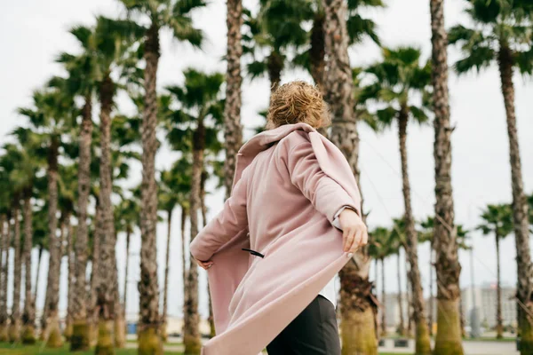 Stijlvolle jong meisje in een roze jas plezier in het park, genieten van de warmte — Stockfoto