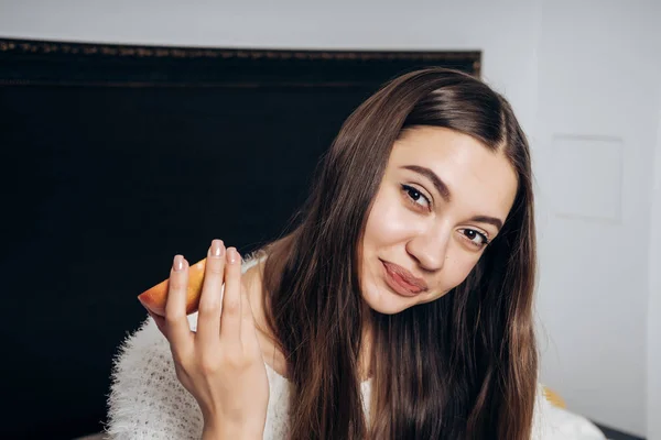 Beautiful cute girl with long hair woke up early in the morning, breakfasts in bed, eating an apple — Stock Photo, Image