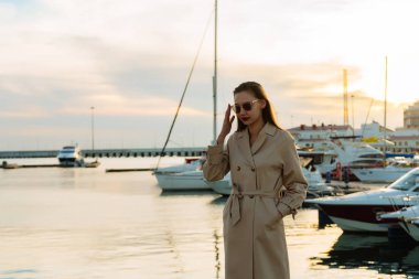 bir lüks şık kız güneş gözlüğü ve bej bir palto onun yat için bekleyen seaport dinleniyor