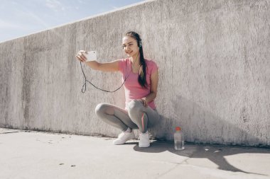 Koşu, kulaklık müzik dinleyip selfies sonra dinlenme spor elbiseleri etkin bir ince kız