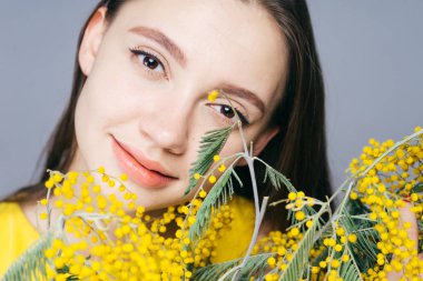 poz ve gülümseyerek, sarı Mimoza tutarak temiz cilt ile çekici güzel kız