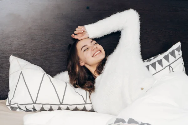 Vrolijk meisje wakker vroeg in de ochtend, ligt onder een witte deken, glimlachen, Goedemorgen — Stockfoto