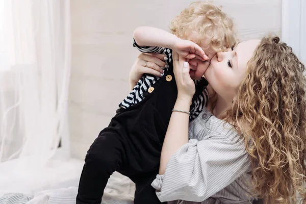 Curly young caring mother kisses her little son, friendly family — Stock Photo, Image