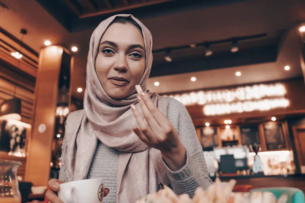 Une fille arabe drôle avec un foulard sur la tête manger de la nourriture savoureuse dans un restaurant, boire du café parfumé — Photo