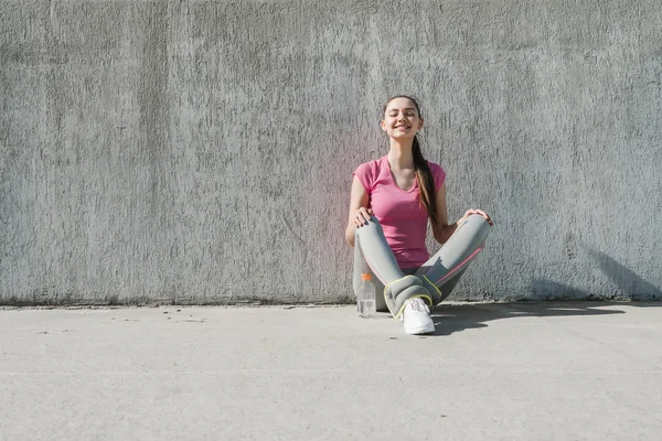 Štíhlé krásnou dívku v Růžové tričko se sedí na zemi venku, odpočívá po běhání — Stock fotografie
