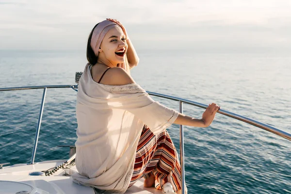Feliz chica con estilo se sienta en un yate blanco, navega en el mar Caribe al atardecer —  Fotos de Stock