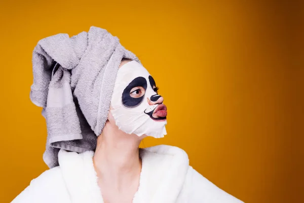 Мила дівчина з рушником на голові доглядає за собою, на її обличчі зволожуюча маска з обличчям панди — стокове фото