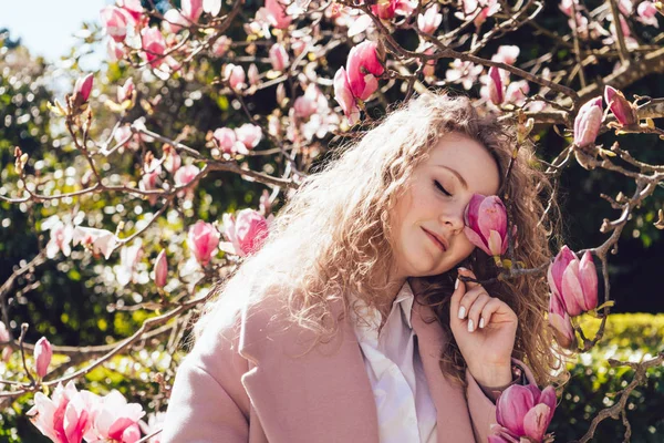 Una mujer rizada de lujo disfruta de una magnolia fragante en un parque de primavera, ama la naturaleza y la calidez — Foto de Stock