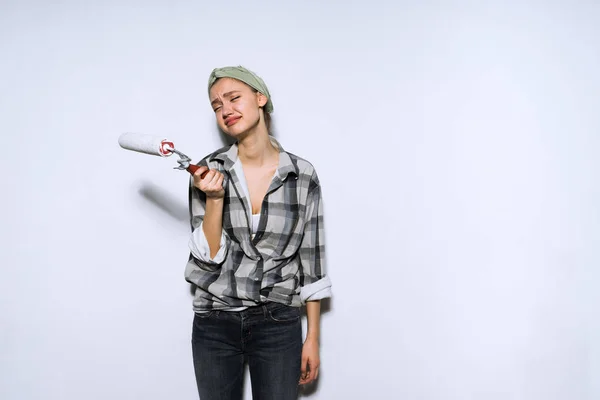 Sad tired girl painter holding a roller for painting the walls, repairing a new apartment — Stock Photo, Image