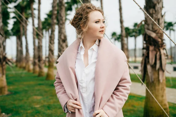 A luxurious stylish woman in a fashionable pink coat walks along the green park, enjoying the spring weather — Stock Photo, Image