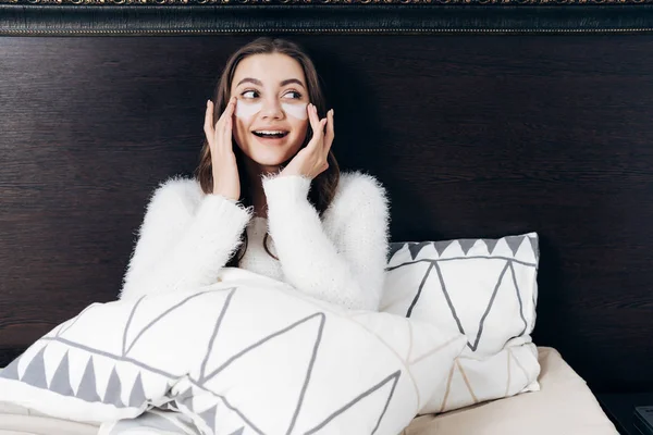 Een charmante meisje ligt in bed onder een deken, onder haar ogen witte patches tegen de zwelling en blauwe plekken — Stockfoto