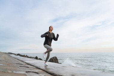 gri spor giyim etkin hızlı kız Denizi çevresinde çalışan, yarışmalar için hazırlar, kulaklıklar müzik dinler