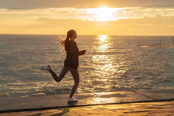 Självsäker smal flicka bedriver jogging på havet vid solnedgången, förbereda för tävlingar på flykt — Stockfoto