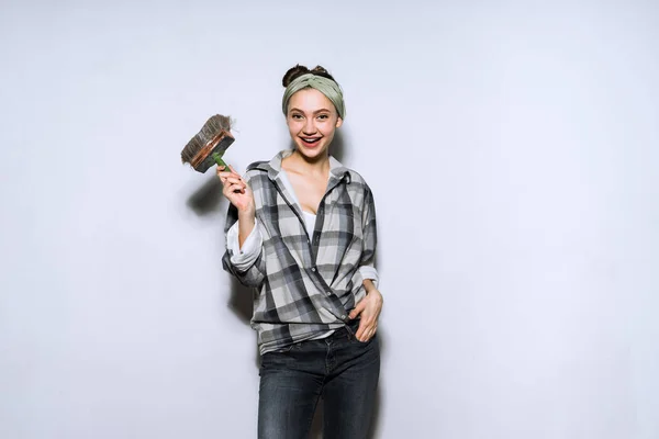 Забавная юная девушка в клетчатой рубашке держит кисть в руке, делает ремонт в квартире — стоковое фото