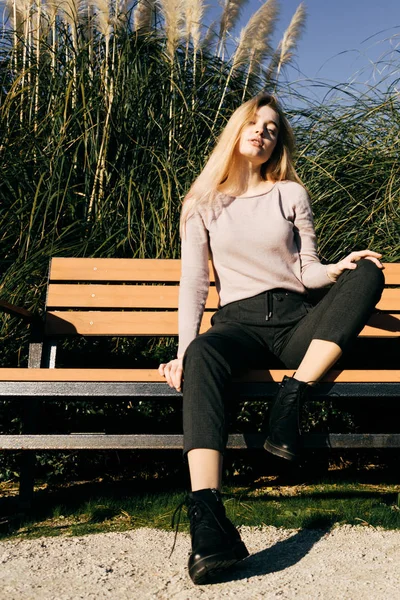 Jovem confiante posando em um banco de madeira no sol, estilo de rua e moda — Fotografia de Stock