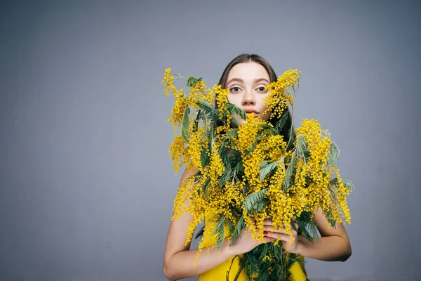Joven hermosa chica posando, sosteniendo un ramo de mimosa fragante amarillo — Foto de Stock