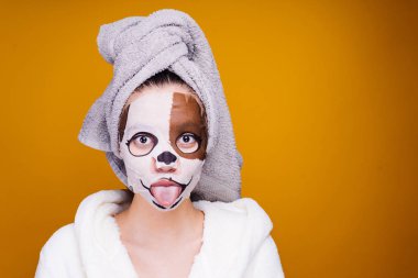 dil, bir nemlendirici maske yüzünde bir köpeğin yüzü olan bir kız beyaz terry sabahlık ve başında bir havlu ile gösterir