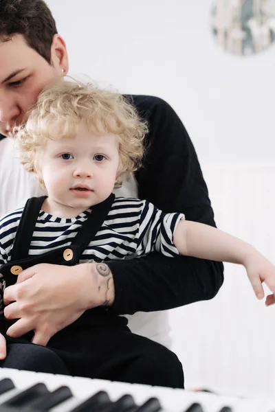 Small curly baby boy sitting in the arms of the pope, playing the piano — Stock Photo, Image