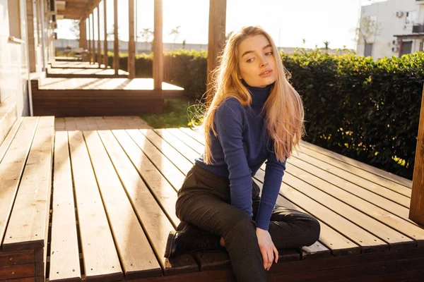 Stylish young blond model girl in blue sweater resting outdoors, sitting on bench — Stock Photo, Image