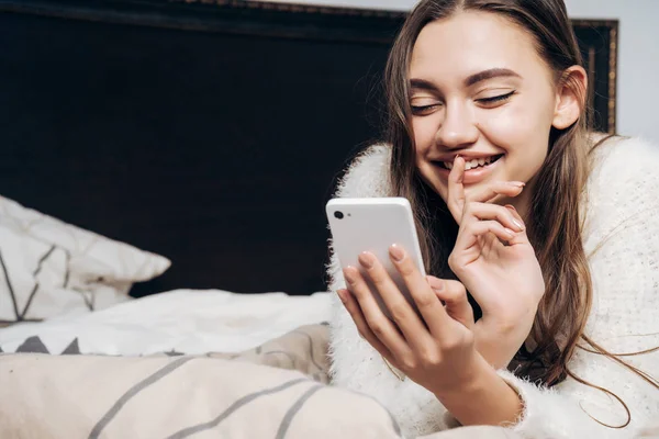 Happy young girl resting after a hard day 's work, looking into her smartphone and smiling — стоковое фото