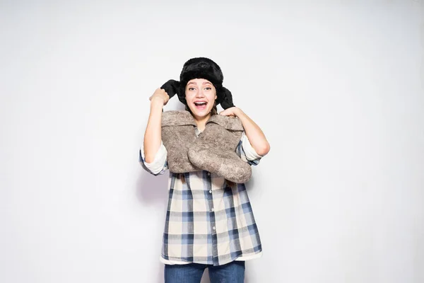 Una alegre chica rusa con coletas, en un cálido sombrero de piel espera el invierno, sostiene botas de fieltro caliente en sus manos — Foto de Stock