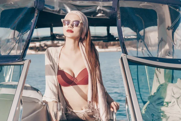 Una mujer atractiva de lujo en ropa de verano y gafas de sol nada junto al mar en su yate, disfruta del sol —  Fotos de Stock